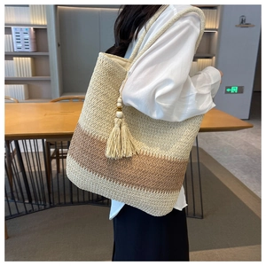 Detail of woven tote bag featuring beige and brown patchwork with tassel accent