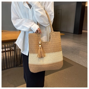 Detail of hand-woven straw tote bag with tricolor patchwork and tassel hanging charm