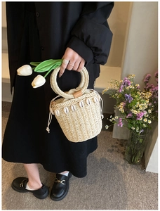 Detail of straw bucket bag with shell ornaments, round handle, and drawstring closure