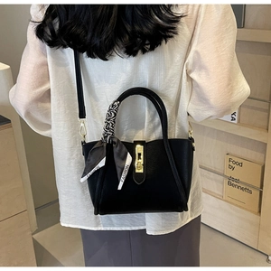 Détail du sac seau noir en cuir avec fermoir doré et poignée ornée d'un foulard en soie