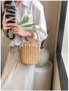 Detail of straw bucket bag with shell decor and ring handles held by a model