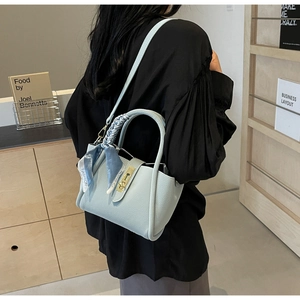 Détail d'un sac seau en cuir bleu clair à motif litchi avec un foulard en soie élégant