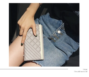 Close-up of light grey quilted long wallet with elegant gold-tone metal edge trim