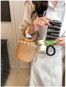 Detailed view of straw bucket bag featuring natural shell decor and drawstring closure
