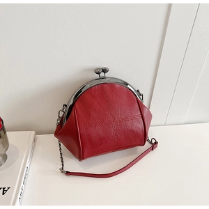Close-up of red lychee grain leather shell bag with metal clasp and cross stitching