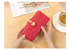 Detail of red long wallet with V-pattern texture and heart-shaped gold metal clasp