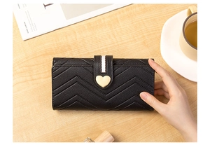 Detail of black chevron quilted long wallet with golden heart clasp on wooden table
