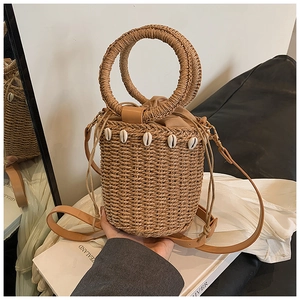 Detail of straw bucket bag featuring seashell decorations and brown PU leather strap