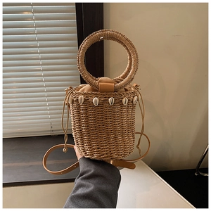 Detail of straw bucket bag featuring white shells and round handle for summer beach style