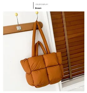Detail of a brown quilted puffer tote bag with thick padded handles hanging on a rack
