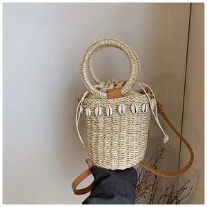 Detail of woven straw bucket bag featuring natural shell decor and drawstring closure