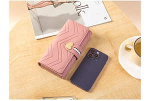 Detail of pink long wallet with chevron quilting and golden heart clasp on wood table