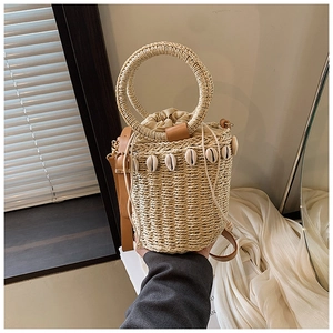 Detail of straw bucket bag with natural shell decor and a brown leather strap