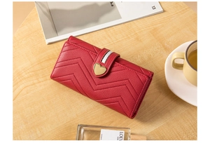 Detail of red quilted leather long wallet with golden heart clasp on a wooden table