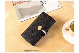Detail of black V-quilted long wallet with gold heart clasp on a wooden desk