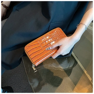 Detail of glossy orange crocodile-patterned long wallet held by a model