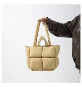 Detail of beige quilted puffer tote bag featuring square padding and dual carry handles