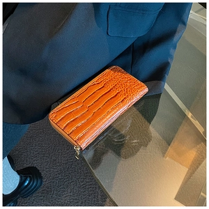 Detailed close-up of glossy orange crocodile texture leather wallet with gold zipper