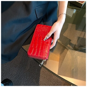 Detail of red crocodile embossed long wallet featuring a silver metal zipper and glossy finish