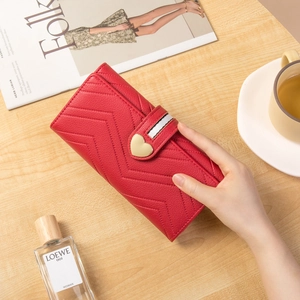 Red long wallet for women with V-quilt pattern and heart-shaped buckle on wood desk