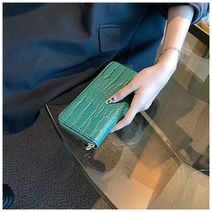 Detail of green crocodile texture long zipper wallet held by a hand in a stylish setting