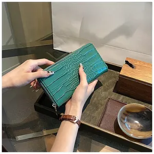 Detail of green long wallet with crocodile embossing and golden zipper in a hand-held view