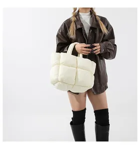 White puffer tote bag with quilted square patterns worn by a model in a brown jacket