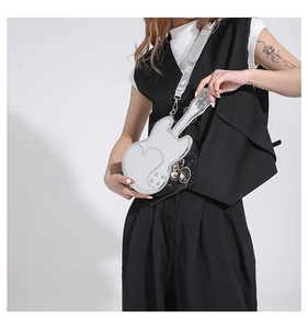Close-up of guitar-shaped silver crossbody bag with heart stitching and tassel detail