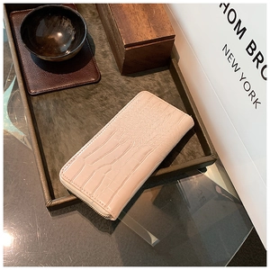 Detail of light pink long wallet with crocodile texture and metal zipper closure