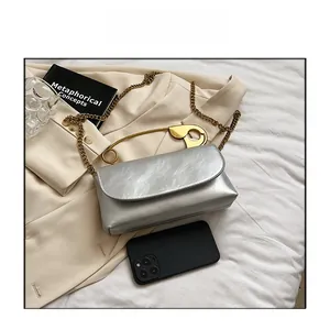 Detailed shot of silver rectangle bag featuring a unique oversized gold safety pin handle
