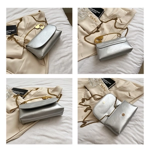 Detail of silver metallic shoulder bag showing magnetic snap and gold safety pin accent