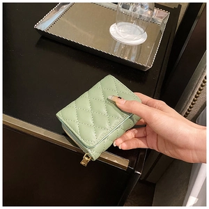 Close-up of hand holding a mint green quilted coin purse with gold zipper on a dark table