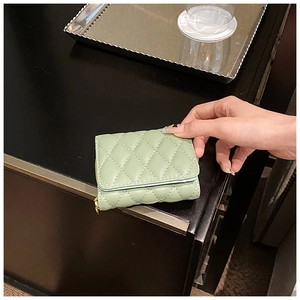 Close-up of light green quilted card holder with gold zipper and diamond stitching detail