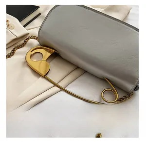 Detail of grey leather bag featuring a large gold safety pin and elegant gold chain