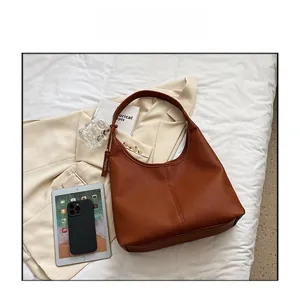Dettaglio di una borsa tote marrone con trama litchi su un letto bianco con accessori