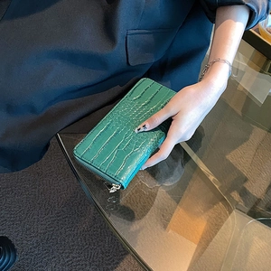 Minimalist green croc-embossed long zipper wallet held by hand in a stylish setting