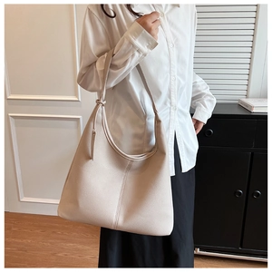 Dettaglio di una grande borsa tote beige con trama litchi e nodo sulla spalla