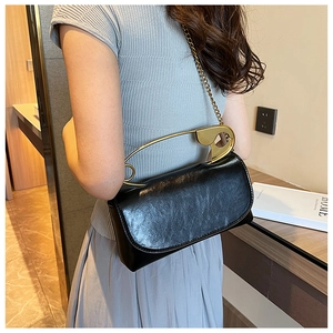 Detail of black leather handbag with unique large gold safety pin handle and chain strap