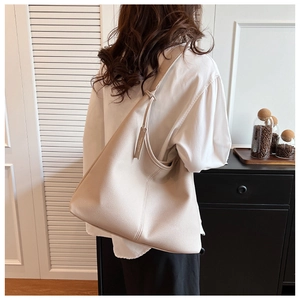 Dettaglio borsa tote beige in pelle grana con ciondolo brand e design hobo minimalista