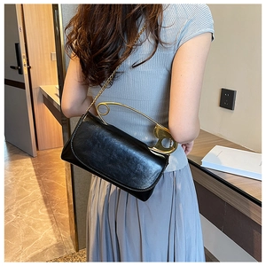 Detail of black leather bag featuring a large gold safety pin handle and chain strap