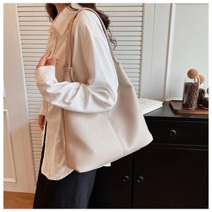 Dettaglio di una grande borsa tote beige con trama litchi sulla spalla della modella