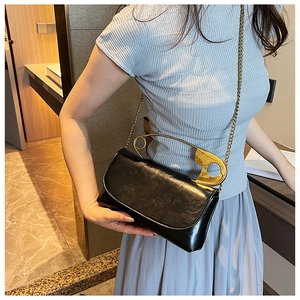 Detail of black glossy shoulder bag with unique oversized gold safety pin handle design
