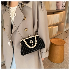 Dettaglio di una borsa da sera nera con strass lucidi, manico di perle e spilla gioiello