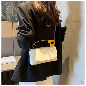 Detail view of a white glossy shoulder bag with a gold safety pin handle and chain strap