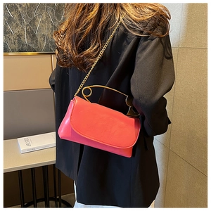 Detail of coral pink crossbody bag featuring unique gold paperclip handle and chain