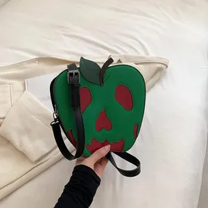 Detail shot of green poison apple crossbody bag with red skull cutout on soft bedding