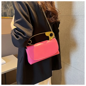 Detail of pink crossbody bag with oversized gold safety pin handle and chain strap