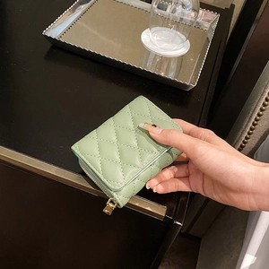 Pale green quilted accordion wallet with gold zipper on a wooden table setup