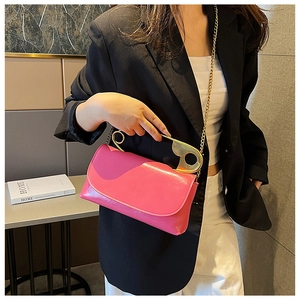 Hot pink crossbody bag with a gold safety pin handle shown on a black blazer