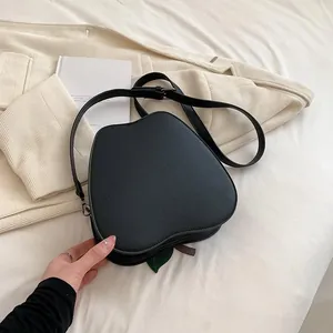 Detail showing the black apple-shaped crossbody bag with leaf accent on fabric background